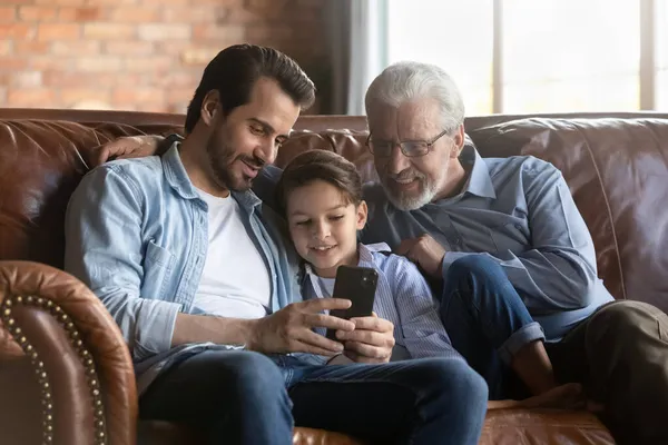 Jubilado abuelo joven padre preadolescente relajarse en el interior utilizar el teléfono inteligente —  Fotos de Stock