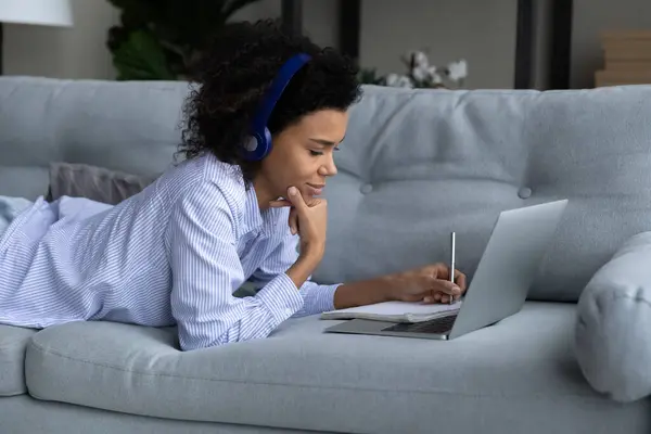 Perfil Mujer afroamericana en audífonos tomando notas, usando laptop — Foto de Stock