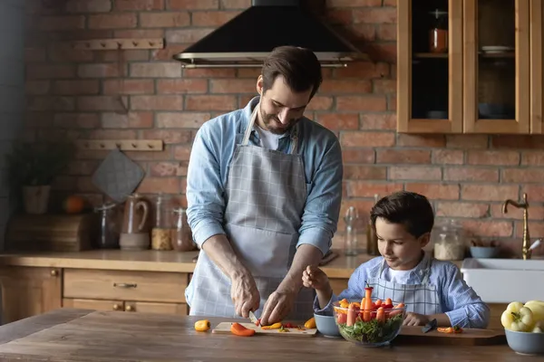 Preteen chlapec imitovat otce při přípravě domácí jídlo zeleninový salát — Stock fotografie