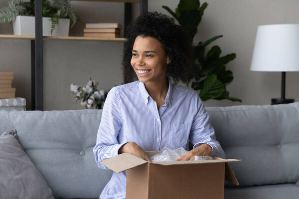 Smiling African American woman customer feeling satisfied, unpacking parcel