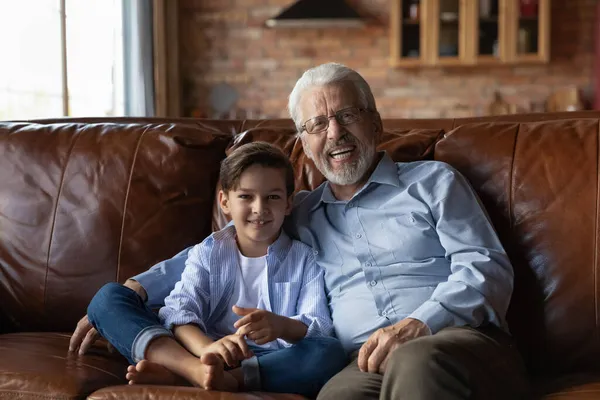 Portrait of elderly grandfather and preschool grandson cuddling on couch — Stock Photo, Image