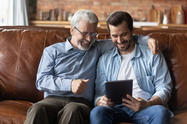 Gözlüklü yaşlı adam yetişkin oğlu ile tablet bilgisayar kullanıyor.