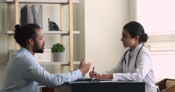 Προσεκτικός νεαρός Ινδός γιατρός ακούγοντας Αφρικανός ασθενής. — Αρχείο Βίντεο
