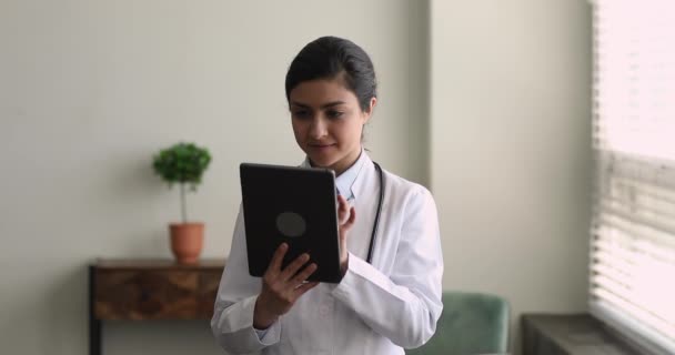 Улыбающийся молодой индийский врач с помощью планшета цифрового компьютера. — стоковое видео