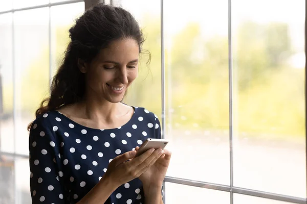 Mujer latina sonriente parada junto a gran ventana de luz uso de teléfono — Foto de Stock