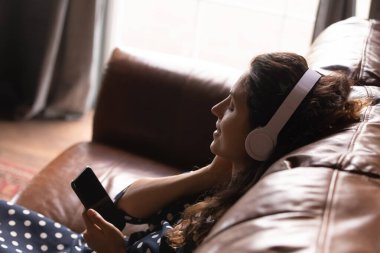 Kulaklıklı rahat genç Latin kadın hücrede podcast 'in keyfini çıkar.
