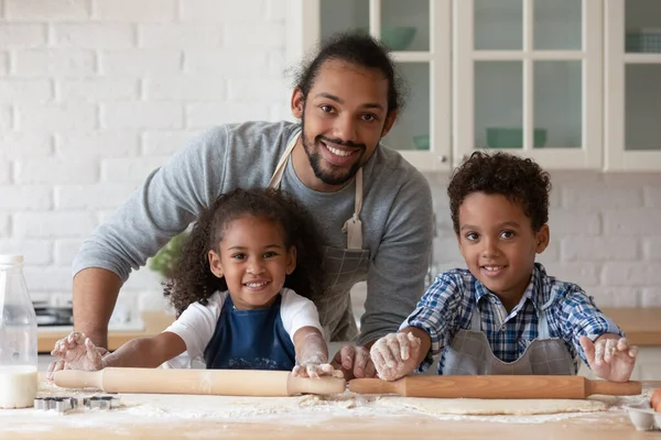 Šťastný černošky táta pomáhá dětem v zástěrách péct koláč — Stock fotografie