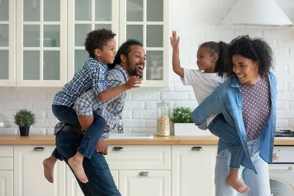 Heureux parents africains actifs piggyback enfants frères et sœurs, courir dans la cuisine — Photo