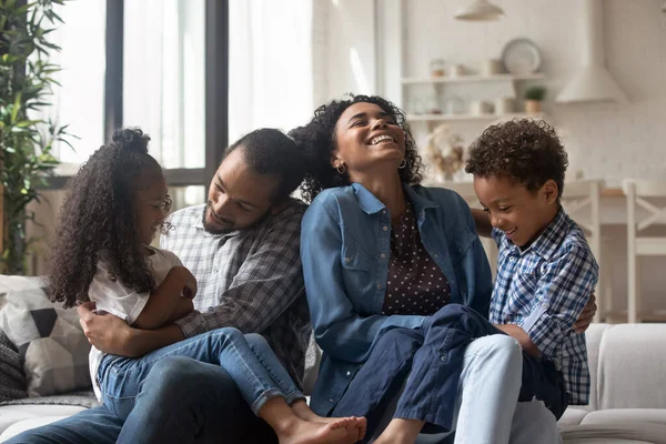 Joyeux jeunes parents noirs câlins, chatouillant les enfants sur le canapé — Photo