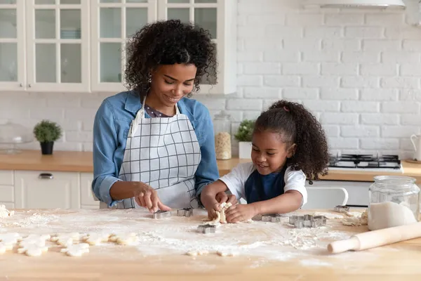 Feliz mamá afroamericana ayudando a linda hija a hornear galletas —  Fotos de Stock