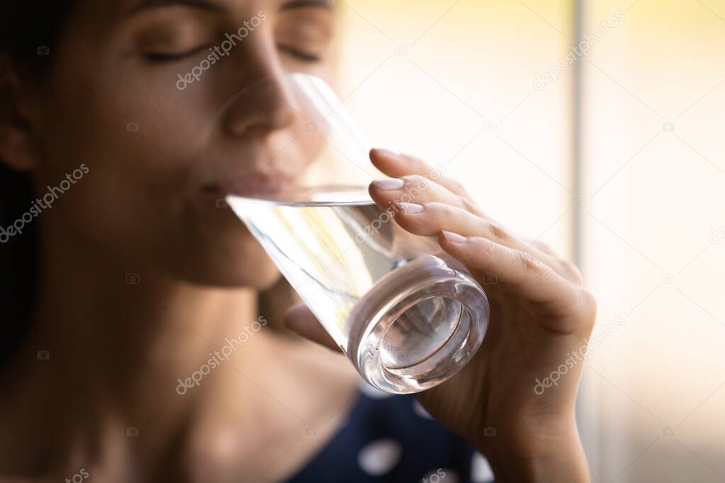 Thirsty millennial hispanic woman drinking cool water with closed eyes