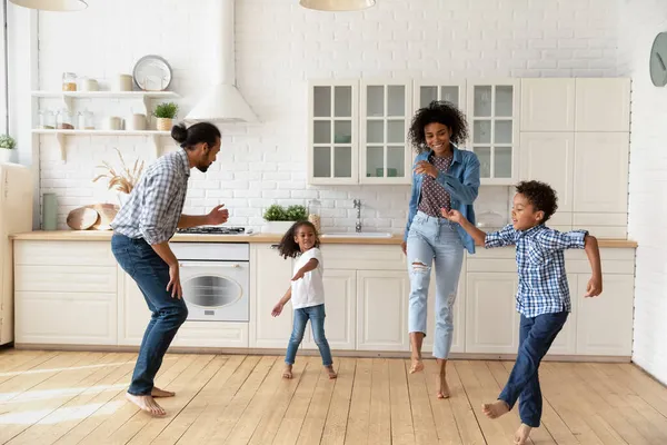 Happy joyful couple and sibling kids dancing rock-n-roll in kitchen — Stock Photo, Image
