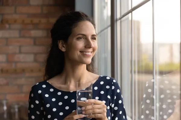 Dreamy young woman begin day from glass of pure water