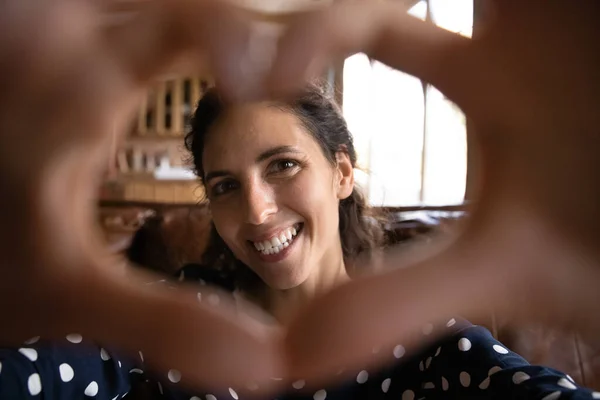 Χαμογελαστή νεαρή γυναίκα κοίτα την κάμερα μέσα από την καρδιά των δαχτύλων — Φωτογραφία Αρχείου