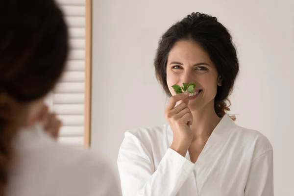 Kobieta w szlafroku patrzeć na aparat wącha zapach pietruszki zioło — Zdjęcie stockowe