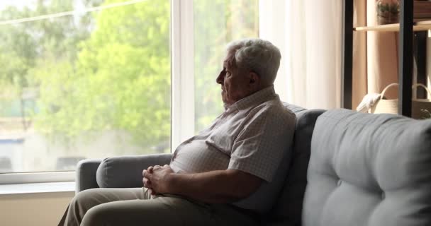 Boldogtalan felnőtt férfi ül a kanapén egyedül néz ablak — Stock videók
