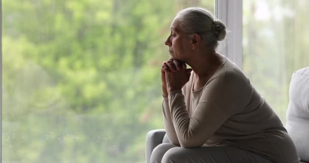 Deprimida mujer mayor sentarse en el sofá en el interior cerca de la ventana de la imagen — Vídeos de Stock
