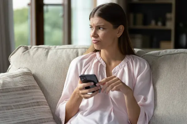 Pensativo infeliz joven mujer usando el teléfono celular en casa. — Foto de Stock