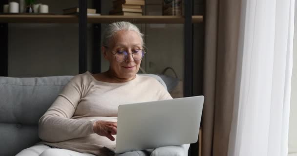 Gealterte Brillenträgerinnen sitzen auf der Couch und arbeiten am Laptop — Stockvideo