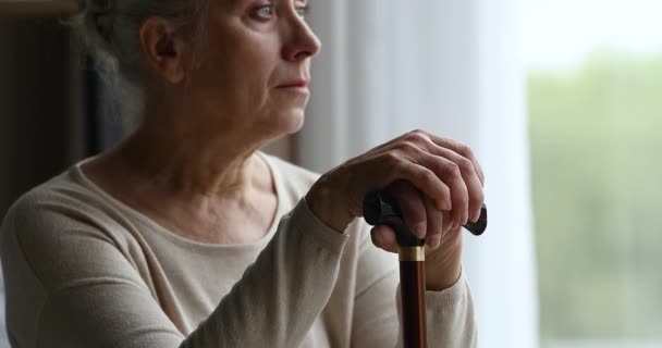 Депрессивная пожилая женщина с ограниченными возможностями сидеть у окна держать палку — стоковое видео