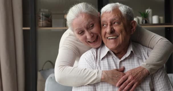 高齢者女性抱擁バックから男座っています上のソファ — ストック動画