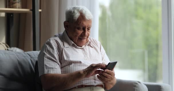 Skrattar äldre hane koppla av på soffan titta på mobilskärmen — Stockvideo