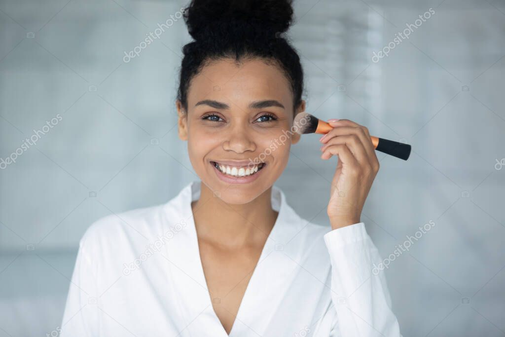 Happy attractive young african woman doing makeup.