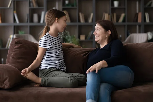 Заботливая взрослая бабушка и внучка разговаривают, сидят на диване — стоковое фото
