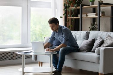 Evde bilgisayar üzerinde çalışan konsantre genç işadamı.