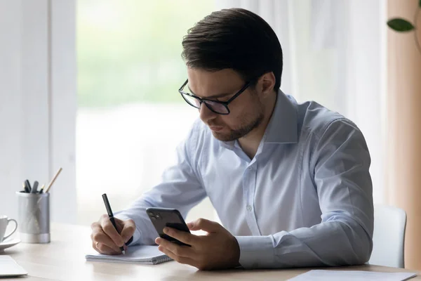 Joven hombre de negocios enfocado escribiendo notas usando teléfono celular. — Foto de Stock