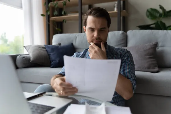 Pensive young businessman reading paper document at home.