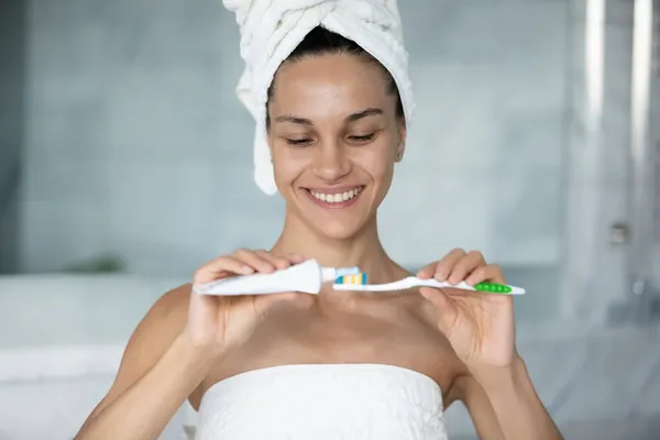 Szczęśliwa młoda latynoska kobieta nakładająca pastę do zębów na szczoteczkę. — Zdjęcie stockowe
