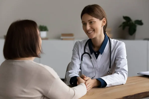 Glimlachende vrouwelijke therapeut arts houden volwassen patiënt handen bij vergadering — Stockfoto