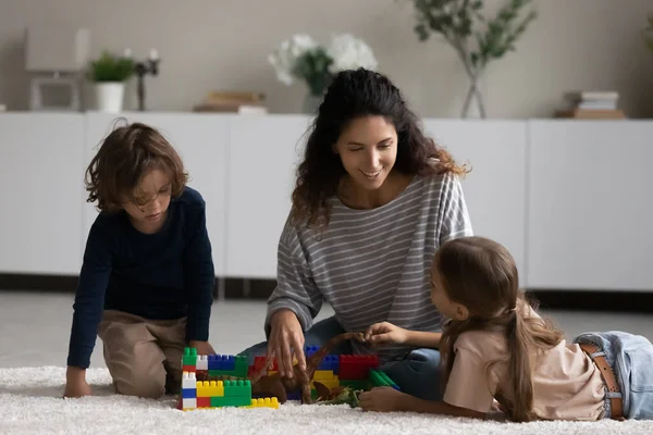 Mère souriante et petits enfants jouant avec des jouets sur le sol — Photo