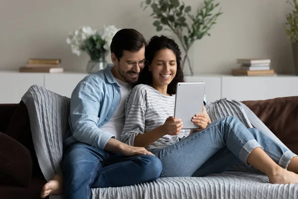 Happy couple hugging, using tablet together, relaxing on couch — Stock Photo, Image