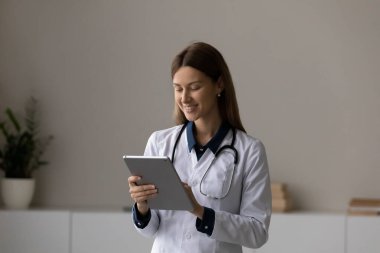 Gülümseyen kadın terapist. Tablet kullanıyor, ofis odasında duruyor.