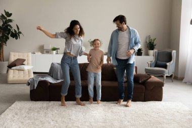 Mutlu ebeveynler ve kızları modern oturma odasında birlikte zıplıyorlar.
