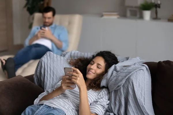 Lächelnde Frau entspannt sich mit Smartphone auf Couch, Paar süchtig nach Geräten — Stockfoto