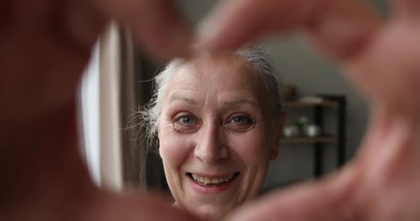 Glimlachen leeftijd oma kijken naar web camera in vinger hart — Stockvideo