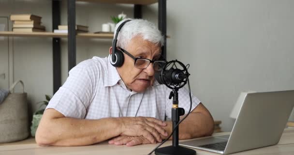 Hombre mayor en auriculares hablan en el micrófono fijado por el ordenador portátil — Vídeo de stock