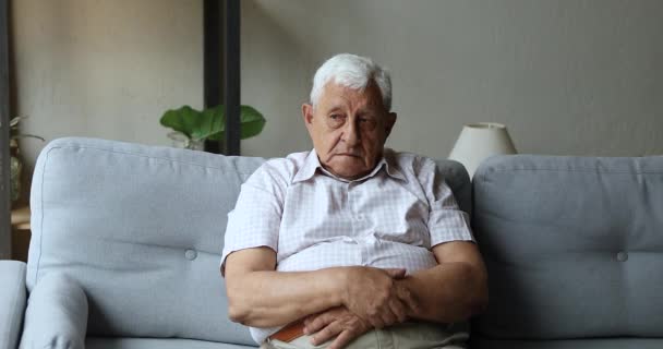 Bedachtzame grijze bejaarde man zit op de bank voel je eenzaam — Stockvideo