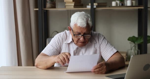 Захоплений чоловік пенсіонер піднімає руку так, читаючи офіційний лист — стокове відео