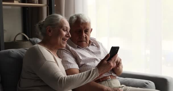 Ενθουσιασμένο ηλικιωμένο ζευγάρι γέλιο αγκαλιά ματιά στην οθόνη του κινητού τηλεφώνου — Αρχείο Βίντεο
