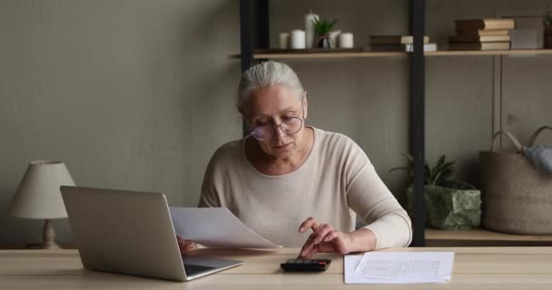 Konzentrierte ältere Dame mit Brille berechnet Dokumente im Home Office — Stockvideo