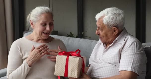 Улыбающийся взрослый седой мужчина преподносит подарок любимой женщине — стоковое видео