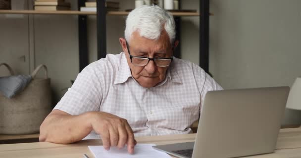생각깊은 나이든 성인 남성이 pc 를 사용하여 종이 문서를 작업하는 모습 — 비디오