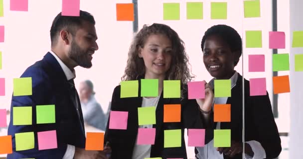 Çok ırklı iş arkadaşları beyin fırtınası yapış yapış notlar üzerine iş stratejisi geliştiriyor — Stok video