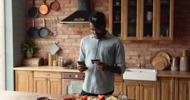 Mutfakta dikilen Afrikalı adam internetten yemek siparişi veriyor.