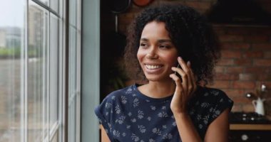 Afrikalı bir kadın mutfakta oturmuş akıllı telefondan konuşuyor.