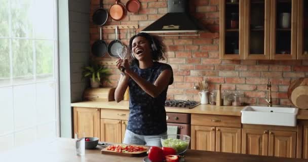 Mujer africana escuchar música a través de auriculares cantando en acogedora cocina — Vídeos de Stock